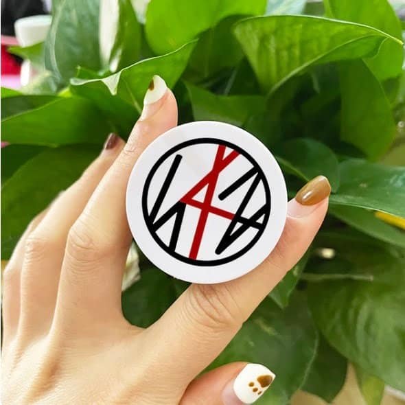 Kpop merch sticker with band logo on a green plant background.