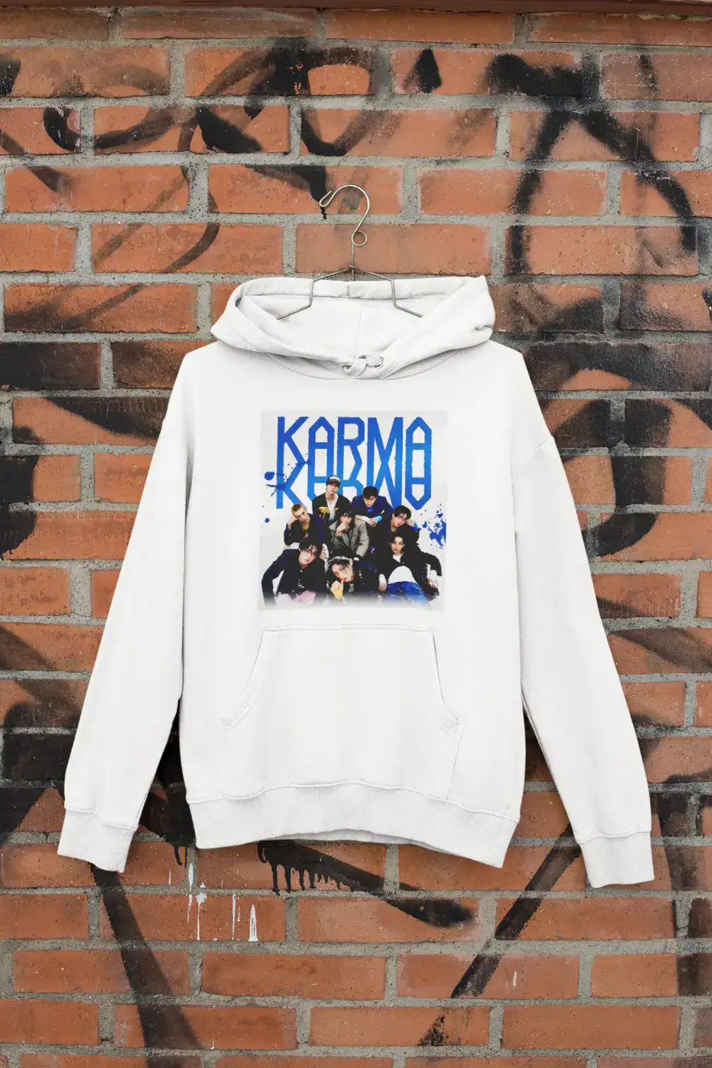 Kpop merchandise hoodie featuring a K-pop group print on the front, hanging against a graffiti-covered brick wall.
